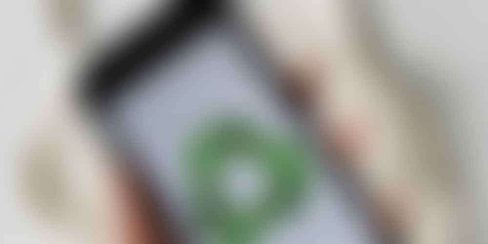 Top view of faceless person holding mobile phone with green recycle logo on white background above cotton eco mesh bag on marble table
